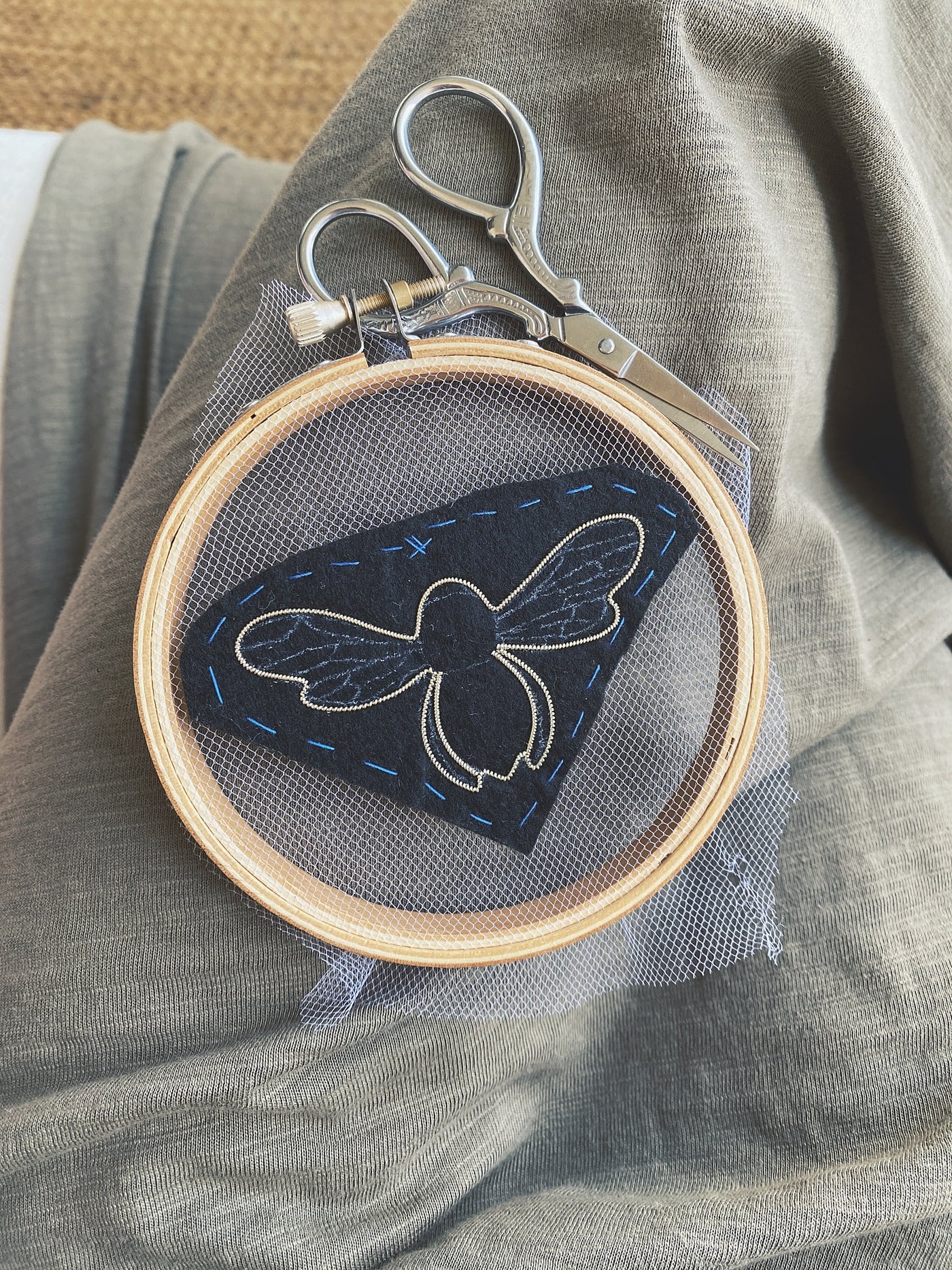 Bastidor con una abeja en proceso, junto a unas tijeras de bordar